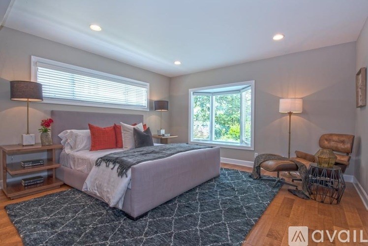 A bedroom with a large bed, a chair, and a window with blinds.