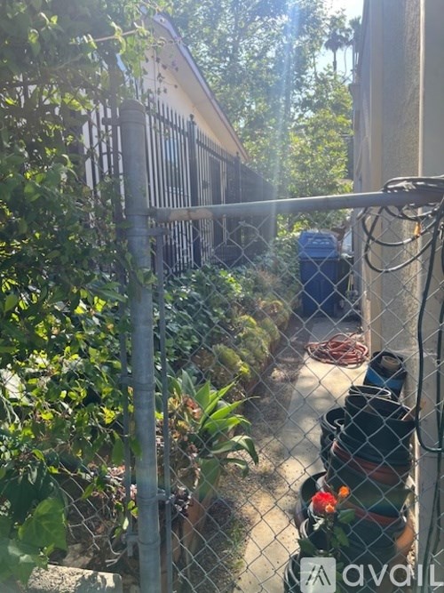 A chain link fence with a gate in the middle separates a lush green area from a building.