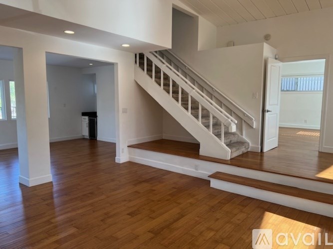 A spacious room with wooden floors and a staircase leading to another level.