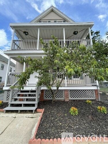 A white house with a porch and a tree in front.