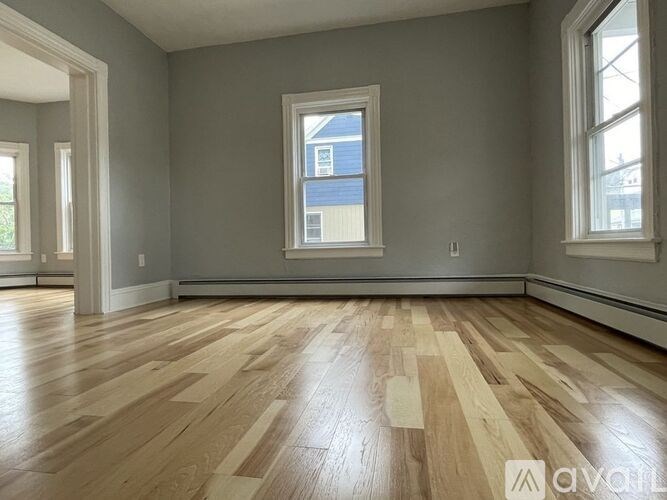 A room with wooden flooring and a window showing a blue building outside.
