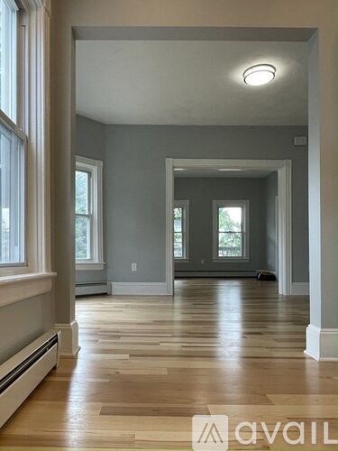 A spacious room with wooden floors and a large window on the left side.