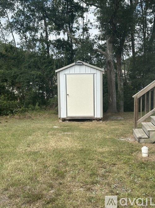 A shed sits in a grassy field with trees in the background.