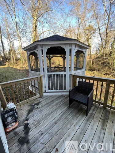 A gazebo with a black wicker chair on a wooden deck.