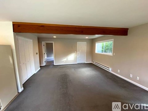 A spacious empty room with a wooden beam ceiling and a window.