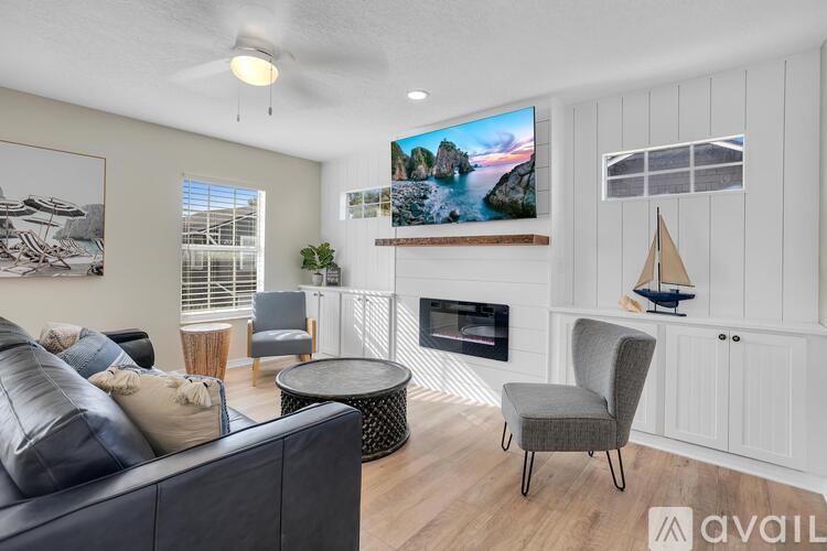 A living room with a grey couch, a black coffee table, a grey armchair, a flat screen TV, and a fireplace.