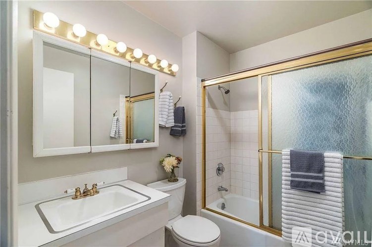 A bathroom with a white sink and a mirror with lights on it.
