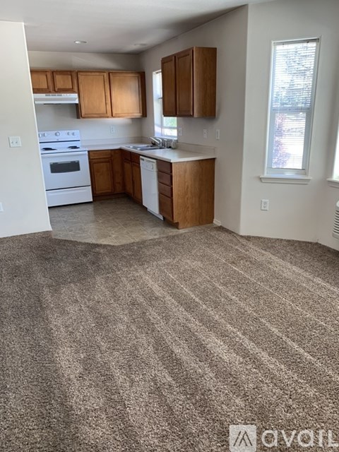 A carpeted kitchen with wooden cabinets and appliances.