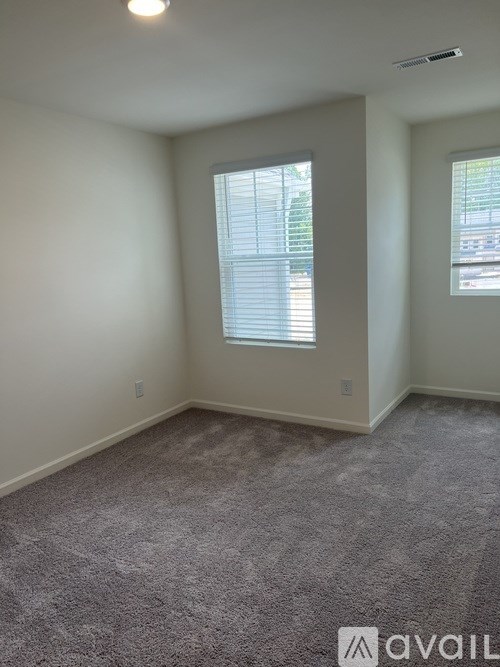 A room with a carpeted floor and two windows.