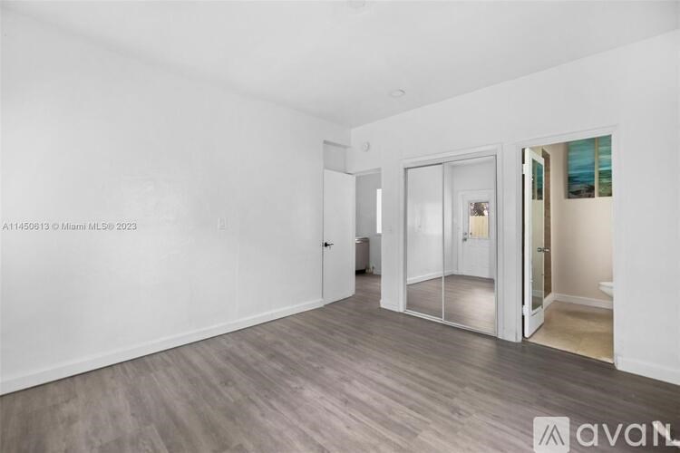 A room with white walls and wooden flooring, with a door and a window.