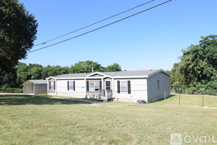 A white mobile home sits in a grassy field with trees in the background.