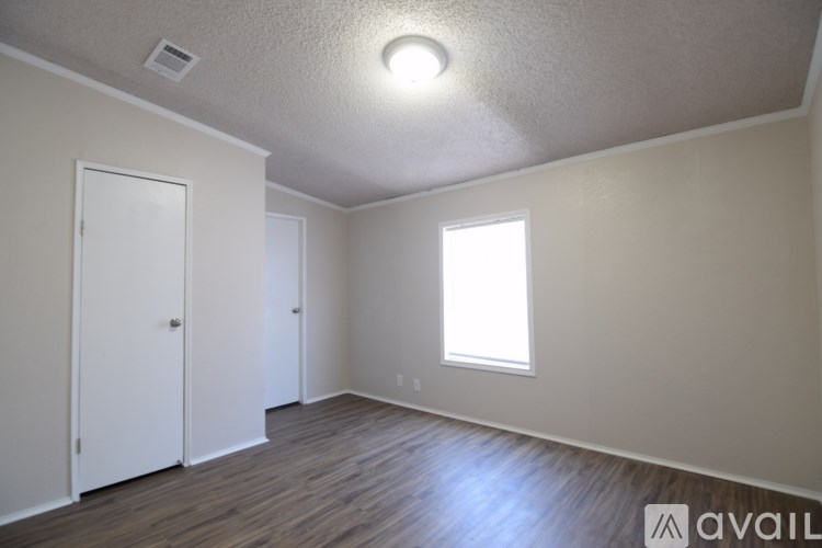 A room with a white door, a window, and a wooden floor.