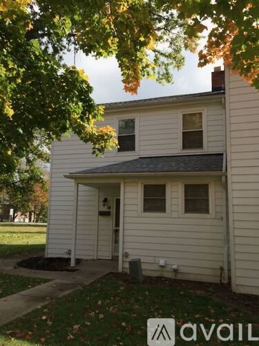 A house with a white siding and a brown roof with a tree in front.