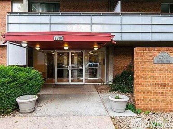 The entrance to a building with a red awning and a glass door.