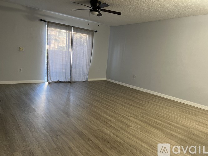 A room with a ceiling fan and light, hardwood floors, and a window with curtains.