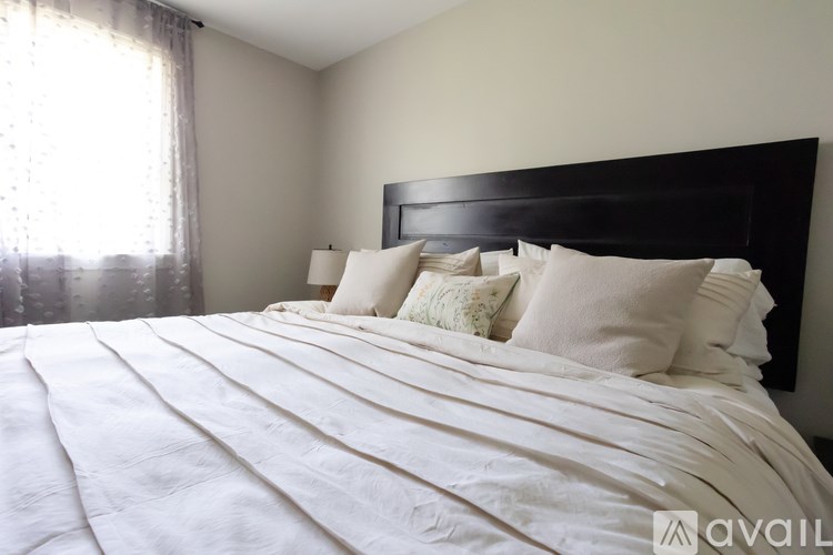 A bed with white bedding and a black headboard is in a room with a window.