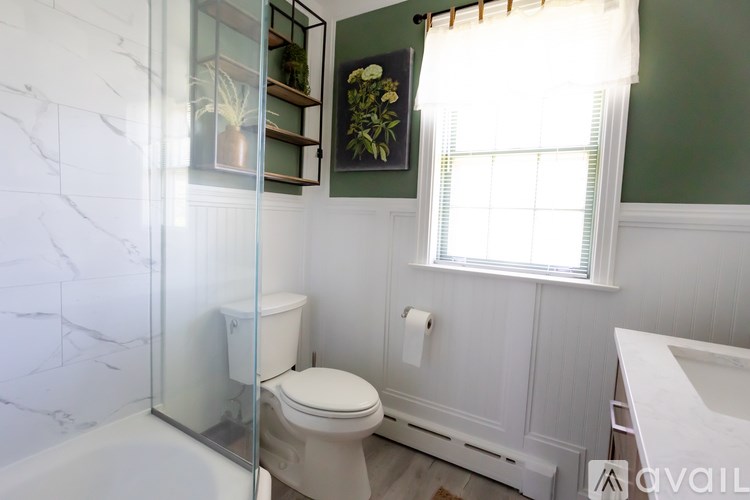 A white toilet in a bathroom with green walls and a glass shower door.