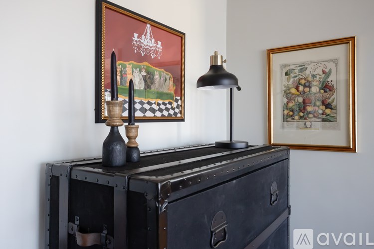 A black chest of drawers with a lamp on top and two framed pictures on the wall.
