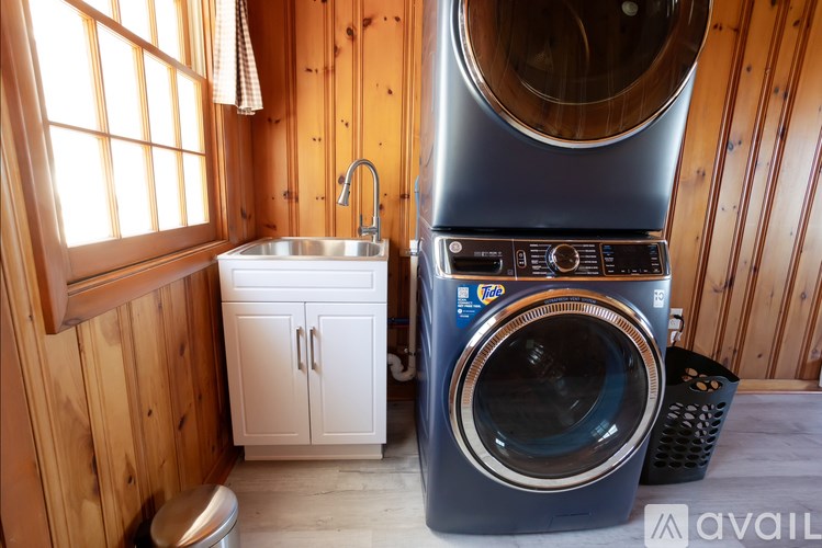 A washing machine is in the foreground of a wooden-walled bathroom with a sink and cabinet.