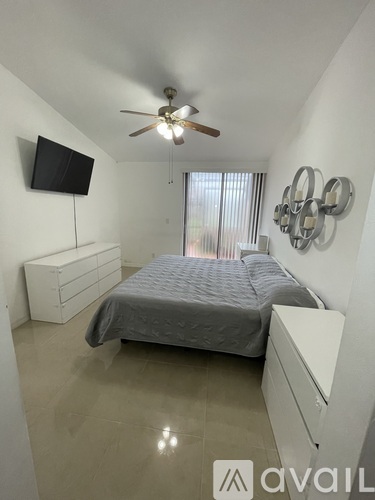 A bedroom with a bed, a ceiling fan, and a television mounted on the wall.