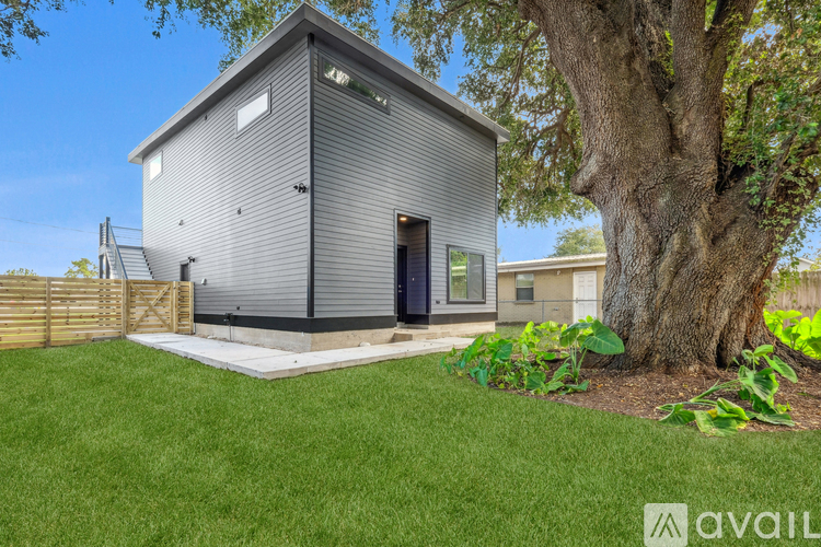 A modern house with a grey exterior and a black door is surrounded by a well-kept lawn and a large tree.
