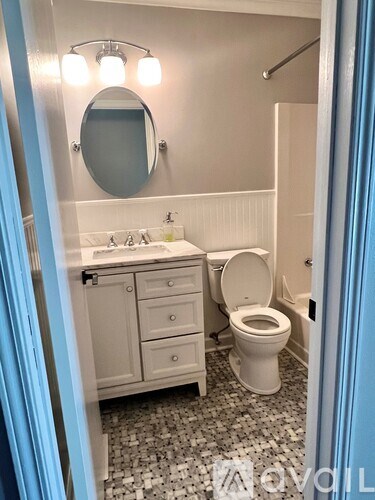 A white toilet is in a bathroom with a white sink and a mirror.
