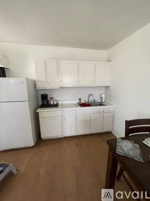 A kitchen with white appliances and cabinets, a wooden table with a glass top, and a chair.