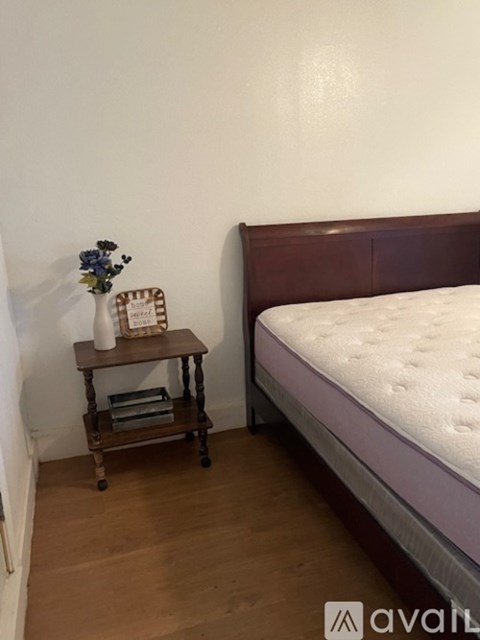 A bedroom with a bed, a small table with a vase of flowers, and a stack of books.