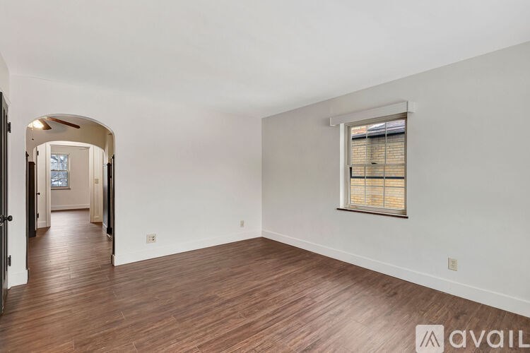 A spacious room with wooden floors and a window with blinds.