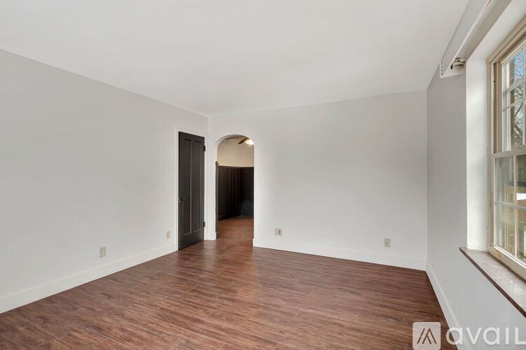 A room with wooden flooring and white walls, with a doorway leading to another room.