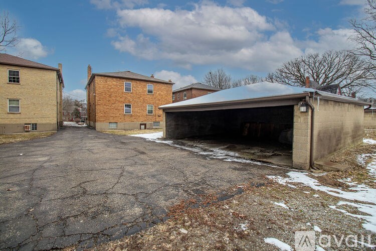 A large, old building with a garage door open is surrounded by a cracked parking lot.