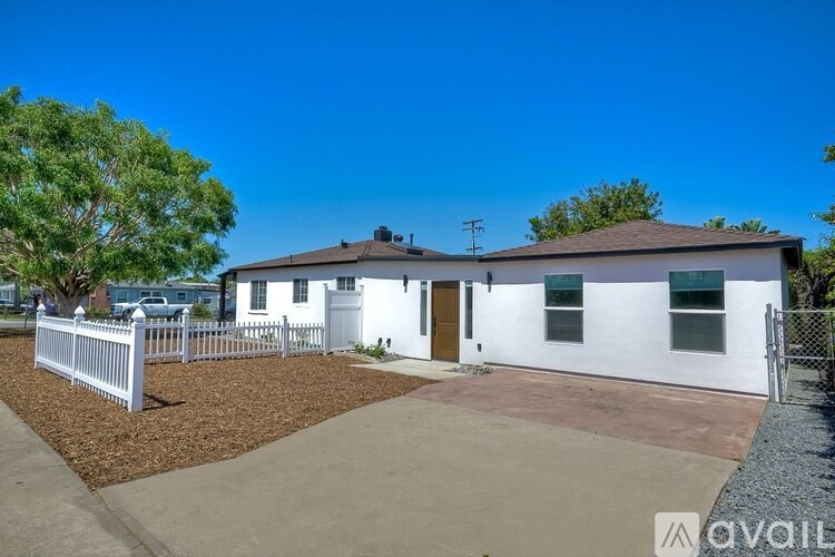 A white house with a brown roof and a white picket fence.