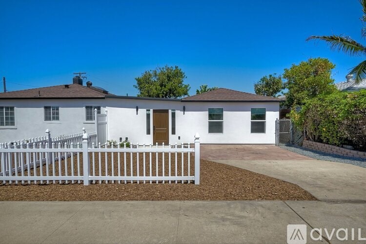 A white house with a brown roof and a white picket fence.
