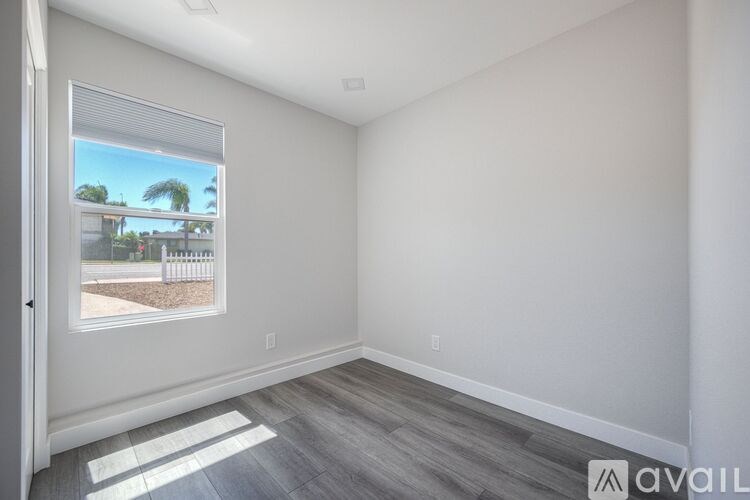 A room with a window showing a view of a house and trees outside.