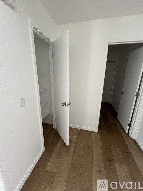 A white door is open to a hallway with wood flooring.