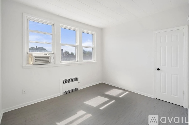 A room with a white door, two windows, and a radiator on the floor.