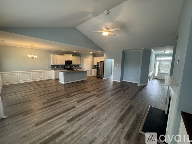 A spacious living room with wood flooring and a kitchen area in the background.