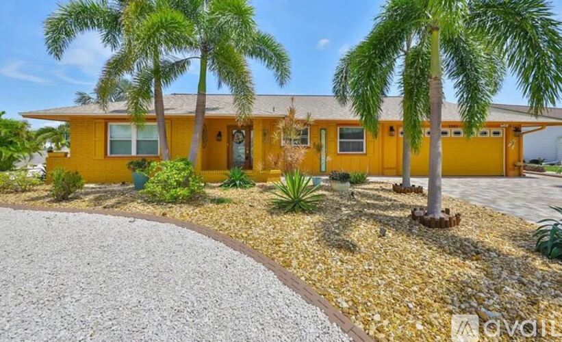A yellow house with a gravel driveway and palm trees in front.