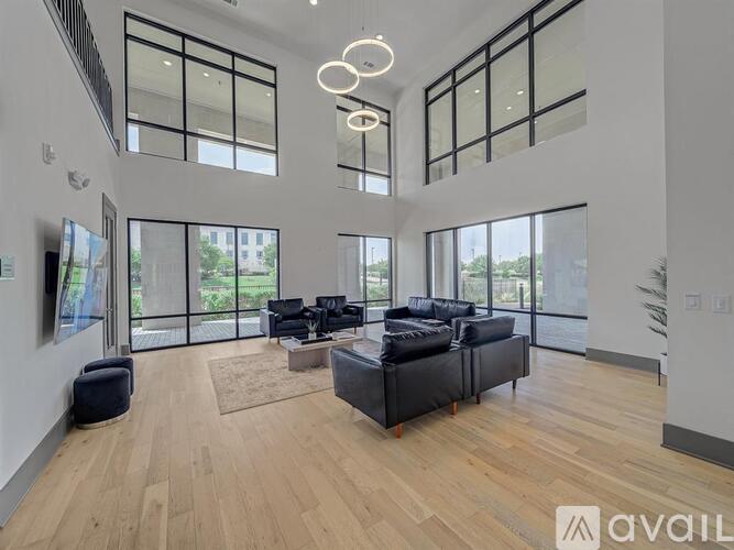 A spacious living room with black leather furniture and wooden flooring.