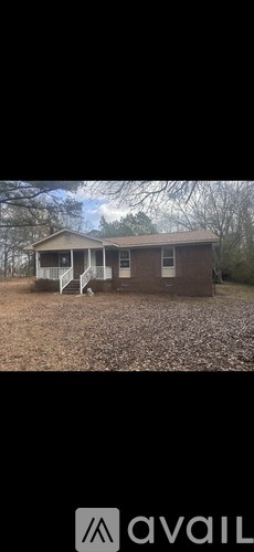 A house with a brown roof and white trim is surrounded by a gravel driveway.