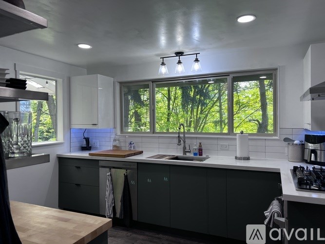 A modern kitchen with a large window overlooking trees.