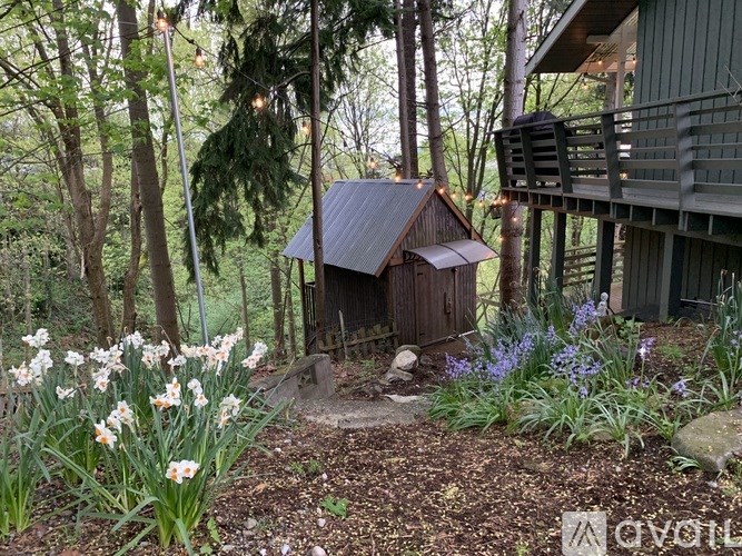 A small wooden shed sits in a garden with a deck behind it.