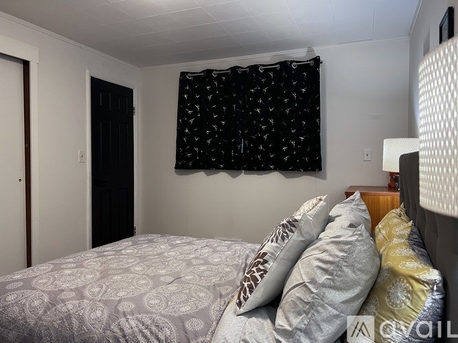 A bedroom with a bed, pillows, and a window with a black and white patterned curtain.