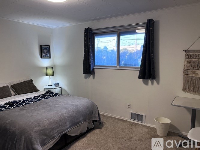 A bedroom with a bed, nightstand, window with curtains, and a picture on the wall.