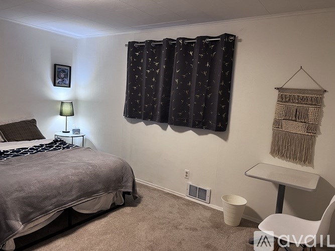 A bedroom with a bed, nightstand, and window with curtains.
