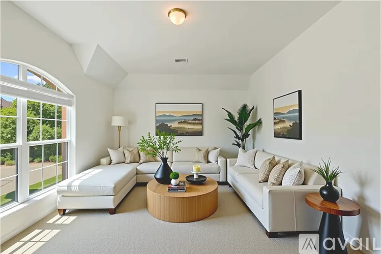 A living room with a white couch, a wooden coffee table, and a large window with a view of the outside.