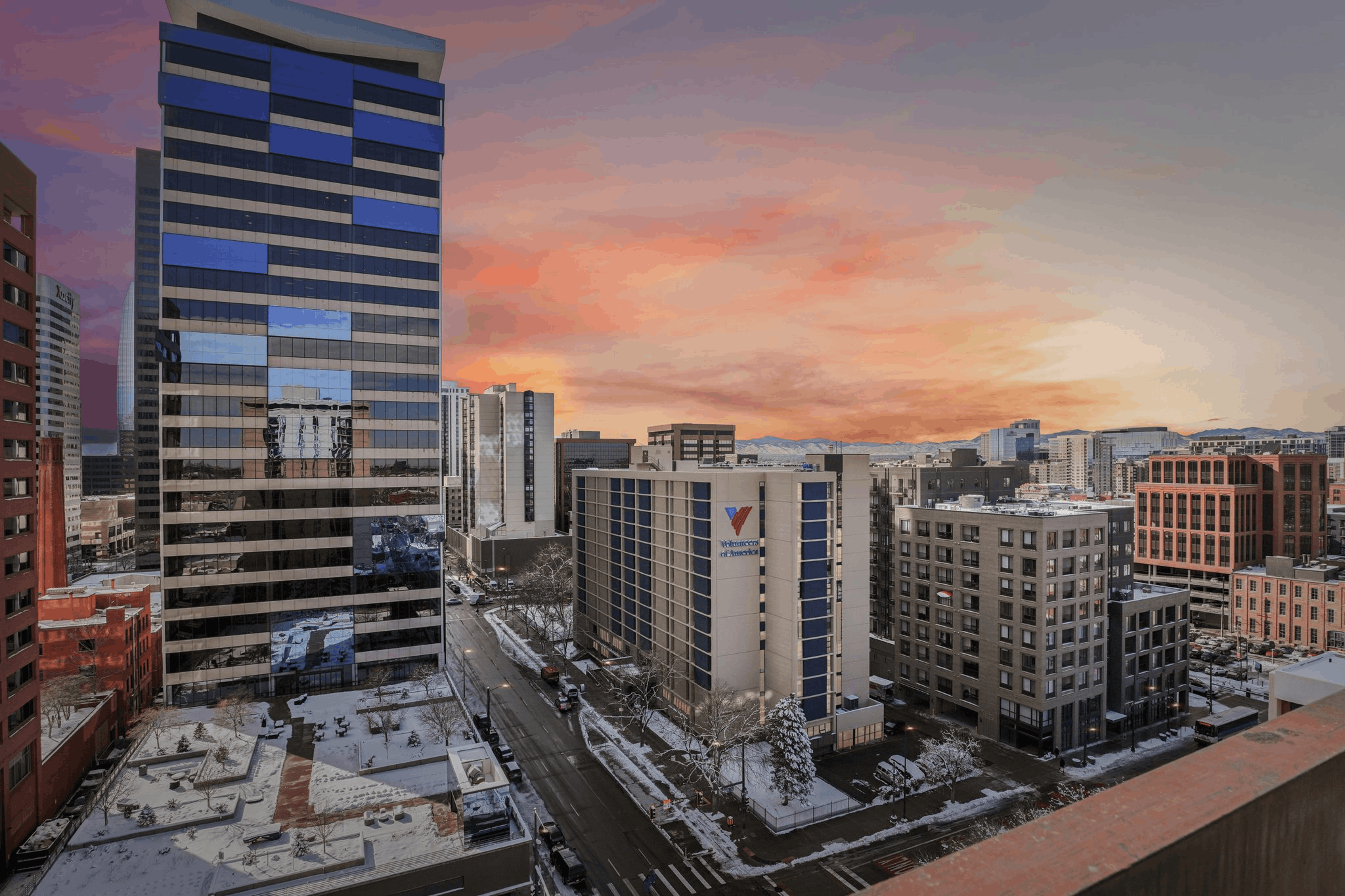 A cityscape with a large building in the foreground and a sunset in the background.