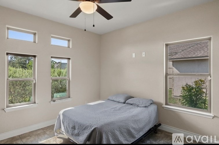 A bedroom with a bed, ceiling fan, and two windows.