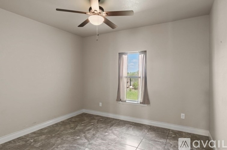 A room with a ceiling fan and a window showing a view of a fence and trees.