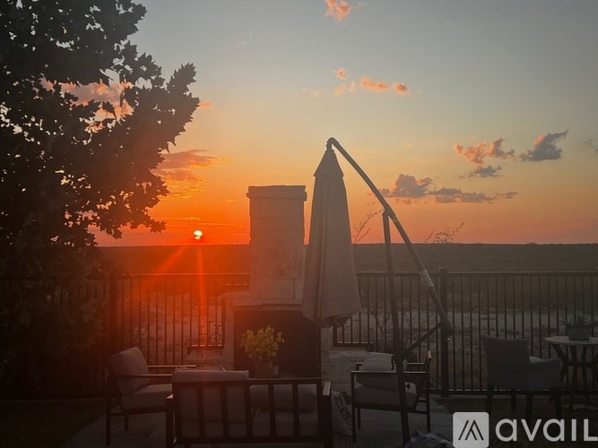 A sunset view from a balcony with a table and chairs.